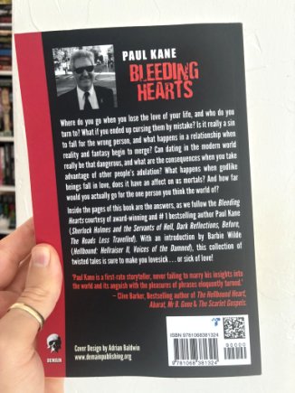 photograph of a man's hand holding up a copy of Bleeding Hearts by Paul Kane, to show the back cover