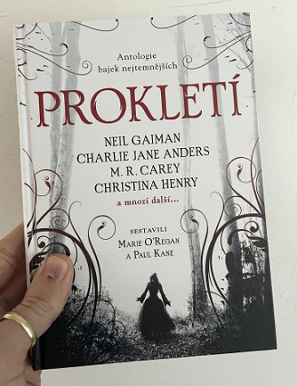 photograph of a man's hand holding up a copy of the Czech translation of Cursed, edited by Marie O'Regan and Paul Kane