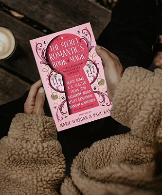 image of someone in a beige fleece jacket holding a copy of The Secret Romantic's Book of Magic, edited by Marie O'Regan and Paul Kane