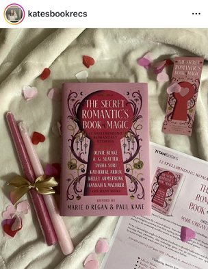 screenshot from @katesbookrecs. Photograph of a copy of The Secret Romantic's Book of Magic, edited by Marie O'Regan and Paul Kane, lying on a cream cloth, alongside the press release for the book, two pink candles tied with a gold ribbon, a Secret Romantic's bookmark, and pink heartshaped confetti